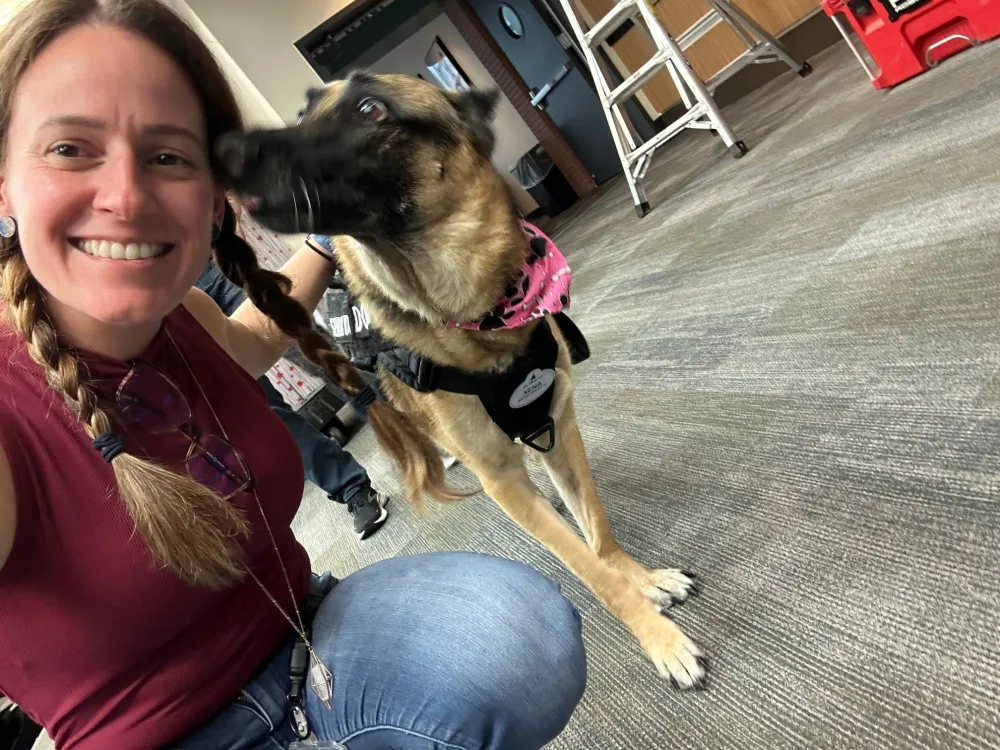 Megan crouching beside Xena, a service dog in a pink bandana