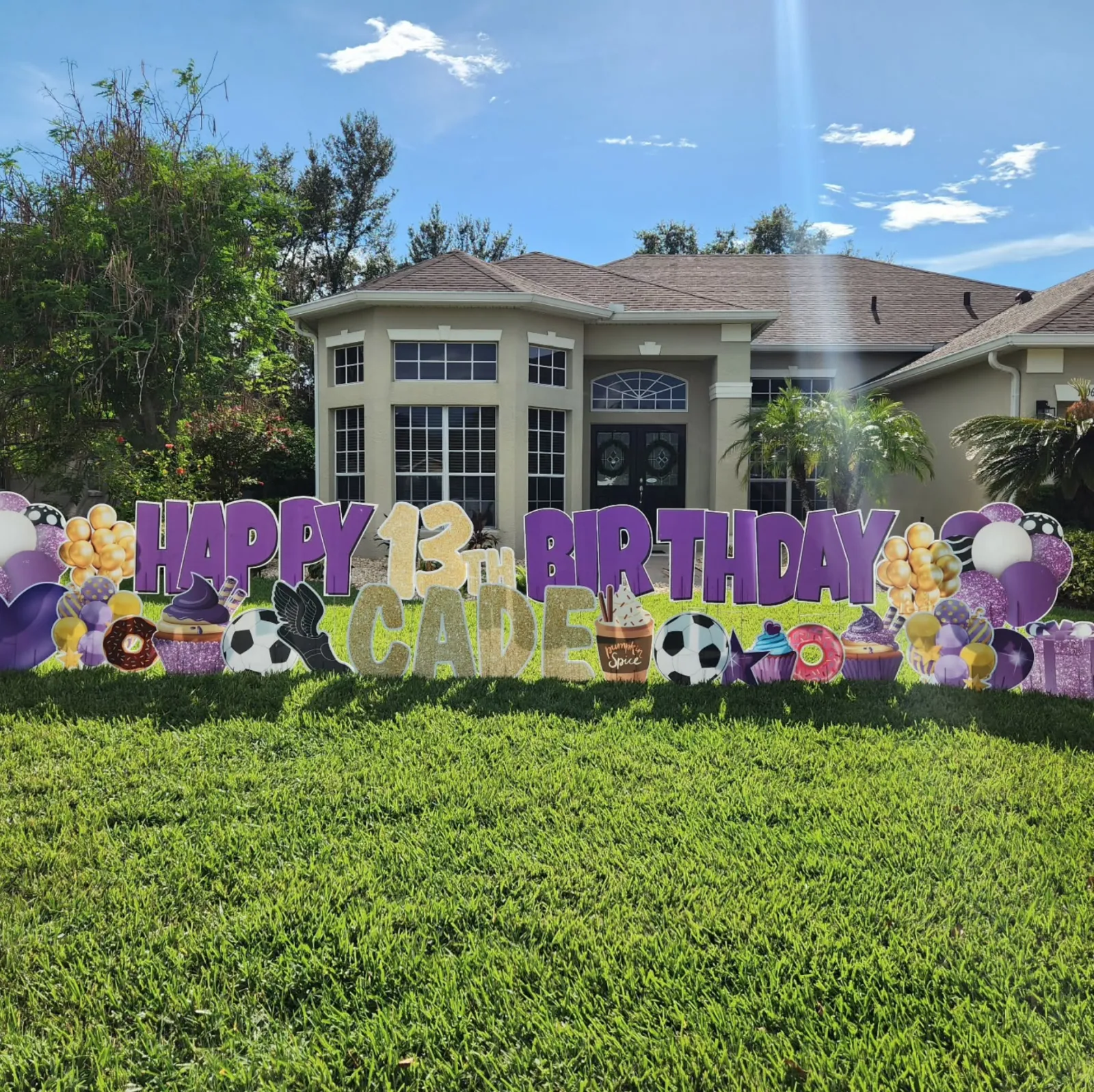 A front lawn decorated with a purple and gold Happy Birthday yard card display